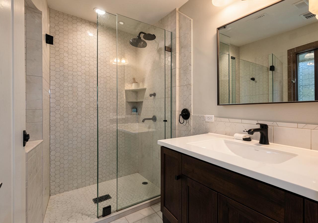 Remodeled bathroom with walk-in glass shower and hexagon tile by First Stop Renovations